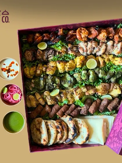 An overhead shot of a large Kebab Box, showcasing the sheer variety and quantity perfect for a party. You can see rows of different kebabs, from paneer tikka to seekh kebabs, ready to be served with dips and breads.