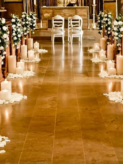 A simple and serene setup for a Christian wedding ceremony. The aisle is lined with candles and white rose petals, leading to two elegant chairs at the altar.