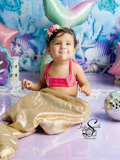 This little mermaid is all smiles. Her golden tail and the sparkling disco balls create a truly enchanting and celebratory atmosphere for her first birthday.