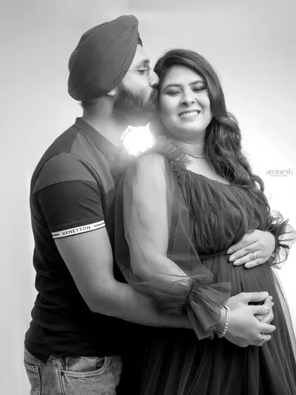 A sweet black and white maternity portrait where the husband kisses his wife's forehead. This classic pose beautifully captures the love and affection between the expecting parents.