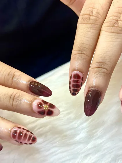 These nails are certified showstoppers. A beautiful and intricate design in deep burgundy, featuring a unique plaid-like texture and floral accents.