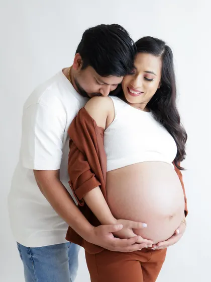 A tender and intimate moment between partners. The dad-to-be gently kisses his partner's shoulder as they both cradle the baby bump.