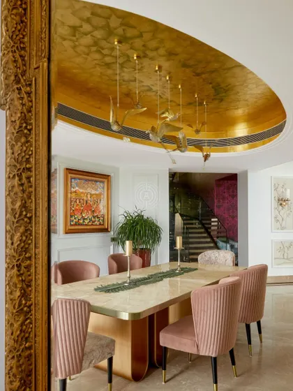 The dining room in the 'Palace in the Sky' home features a gold-leafed ceiling and a custom chandelier of flying birds by Klove Studio. The pink pleated chairs and marble table create a regal yet modern dining experience.