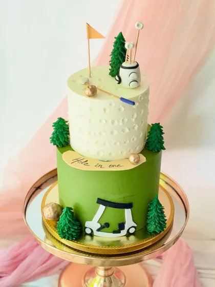 A "hole in one" celebration cake for a golf enthusiast. This two-tiered design features a dimpled top tier, a golf cart, and other course details made from fondant.