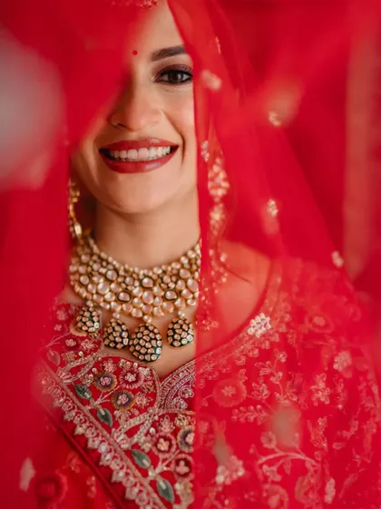 A close-up of the bride smiling through her red veil. This intimate shot captures her joy and the vibrant color of her traditional attire.