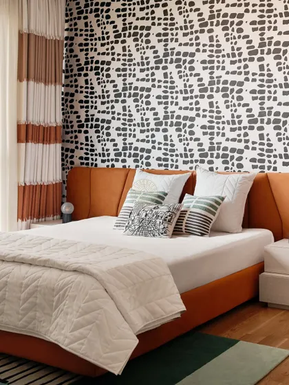This bedroom makes a bold statement with a graphic black-and-white patterned wall behind an orange upholstered bed. The striped curtains add another layer of pattern, creating a vibrant and energetic space.