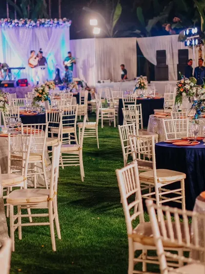 An outdoor reception with a live band on stage. The tables are set with a mix of silver and navy blue linens, creating a sophisticated color palette against the green lawn.