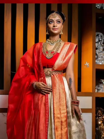 This coordinated couple's outfit features a stunning red and cream half saree for her, designed to complement his look for a photoshoot or event.