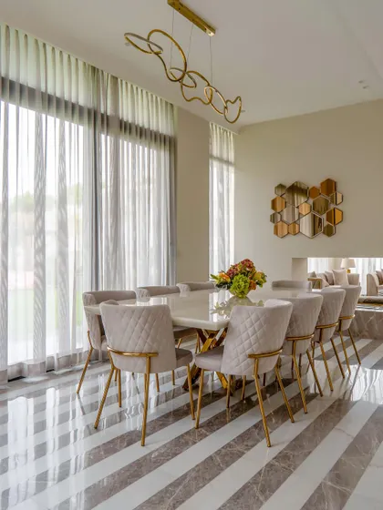 A wide shot of the elegant dining room, showcasing the striped marble floor, modern chandelier, and a view into the adjacent living area. The neutral color palette creates a calm and sophisticated atmosphere.