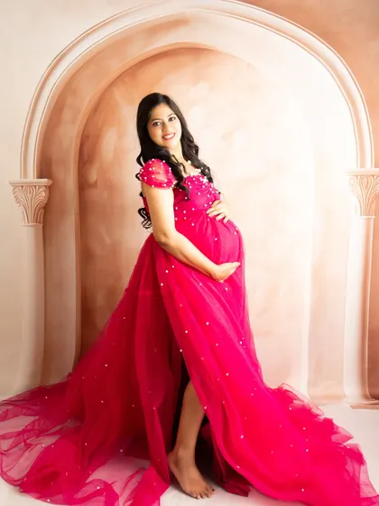 A happy and confident pose in a pearl-studded pink gown. The classic studio backdrop keeps the focus entirely on the mother-to-be.
