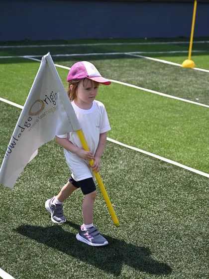A student proudly carries the Knowledge Origin flag during the opening march past.