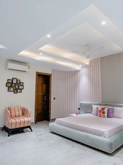 A wider view of the pink bedroom, showing the spacious layout and the single striped armchair that adds a playful contrast.