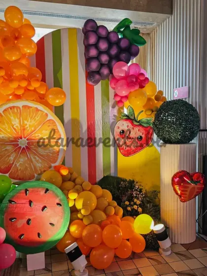 I use a mix of textures and shapes, from balloon grapes and oranges to a smiling strawberry, to build a multi-layered and visually engaging backdrop for the celebration.