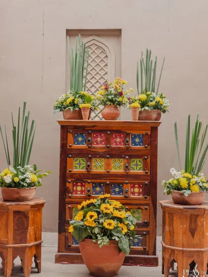 A rustic and charming decor corner for a Jaipur wedding, featuring sunflowers and other yellow blooms arranged in terracotta pots on a traditional tiled chest of drawers.