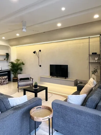 An overview of a living room designed for comfort and style. The space features plush grey sofas, a piano nook with an arched detail, and a floating TV unit with integrated lighting.