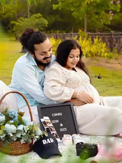 A lovely wide shot of the couple's picnic. The lush green grass and the thoughtfully placed props create a beautiful and relaxed atmosphere for their maternity photos.
