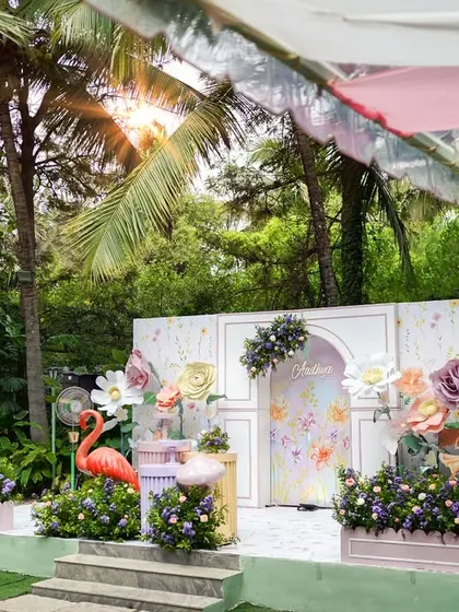 The main stage for the fairy garden party, featuring a whimsical backdrop, oversized flowers, and a playful flamingo prop. The design combines soft colors with lush greenery to create a beautiful outdoor setting.