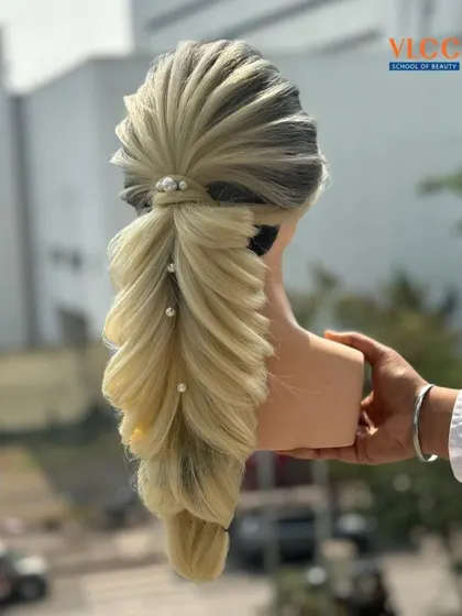 A demonstration of a stunning pull-through braid on a blonde mannequin. The style is accented with pearls, showcasing how to create voluminous and visually complex braids.