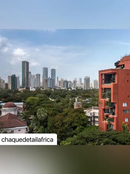 Another perspective of the tower rising above the trees, with the Mumbai skyline in the distance. The terracotta color provides a warm, earthy contrast to the sky and surrounding buildings.