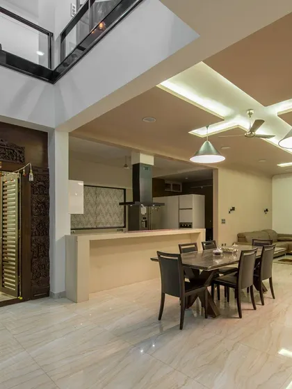 This image captures the grand scale of the open-plan living area, anchored by the traditional puja room. The double-height ceiling over the mezzanine level adds to the sense of volume and architectural drama.