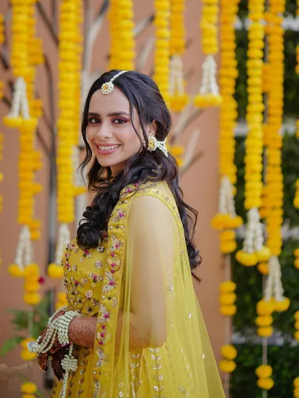 A smiling portrait of Dr. Archita against the marigold backdrop. Her makeup is vibrant and perfect for the occasion.