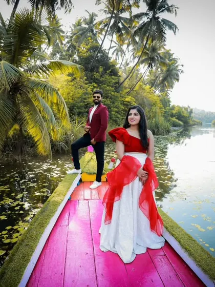 A stunning pre-wedding shoot on a boat. The bride-to-be is wearing a custom red and white Indo-Western outfit that looks incredible against the lush green backdrop.