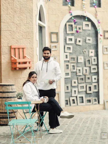 A relaxed portrait of the couple at a studio cafe set, looking confidently at the camera.