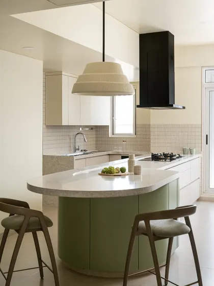The kitchen island is the hero of this space, with its gentle curve, soft green base, and a large, tiered pendant light hanging above.