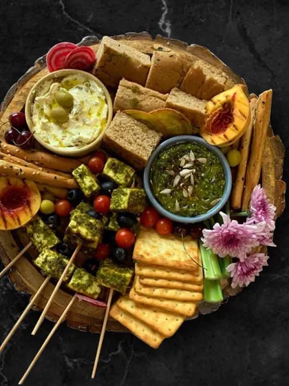 My Italian Platter is a celebration of Italian flavors. It features pesto-grilled tofu skewers, focaccia bread, assorted crackers, a fresh pesto dip, and a creamy olive and feta dip, garnished with fresh tomatoes and olives.