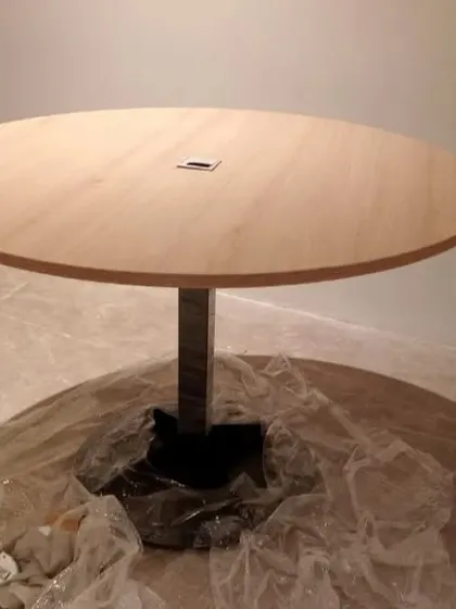 A close-up of a round office discussion table during installation, showing the wooden top and sturdy metal base.