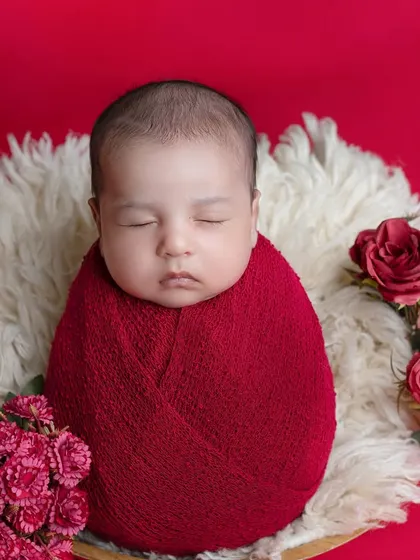 A bold and beautiful setup with a newborn wrapped in red, surrounded by matching roses.