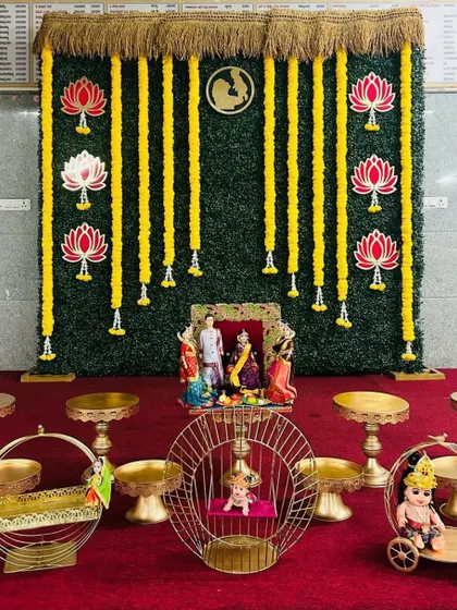 A clear, straight-on shot of a Seemantham stage. This image clearly shows the greenery wall, marigold garlands, lotus cutouts, and the arrangement of traditional dolls and props.