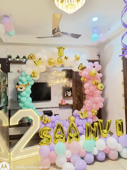 A beautiful pastel-themed 2nd birthday for "SAANVI". This living room setup includes a balloon arch in mint, pink, and lavender, gold foil name balloons, and a large light-up number '2'.