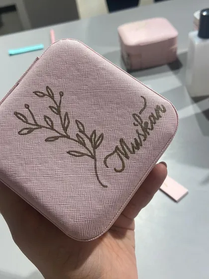 Here is a detailed view of a personalized jewelry case. I hand-drew the name 'Muskan' alongside a botanical design, creating a soft and elegant look on the pink faux leather.