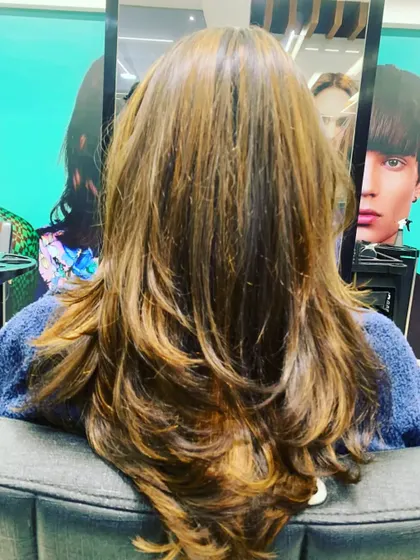 This client's long layers are enhanced with warm, golden-brown highlights. The color adds depth and movement, preventing long hair from looking flat.