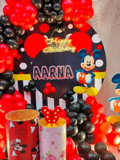 A Mickey Mouse themed birthday party with a red and black balloon arch. The setup includes a custom backdrop and Mickey-themed pedestals.