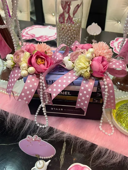 Details are everything in a themed tablescape. For this coquette design, I created a centerpiece by wrapping fashion books with polka-dot ribbons, pearls, and flowers, blending literary charm with feminine romance.