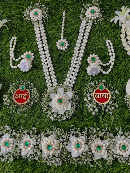 A close-up of a custom Dohale Jevan set with green stone accents. The set includes personalized 'Aai' and 'Baba' brooches, a kamarband, necklace, and earrings.
