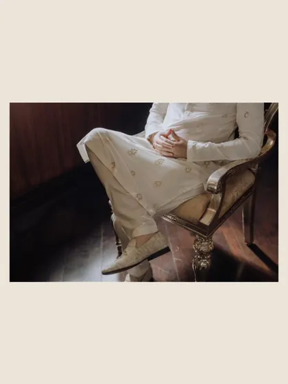 A detailed, artistic shot focusing on the groom's traditional shoes and the lower part of his attire as he sits in a gilded chair.
