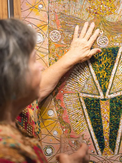 A close-up of artist Eva Malhotra's hand on one of her carved paintings, illustrating the tactile nature of her art.