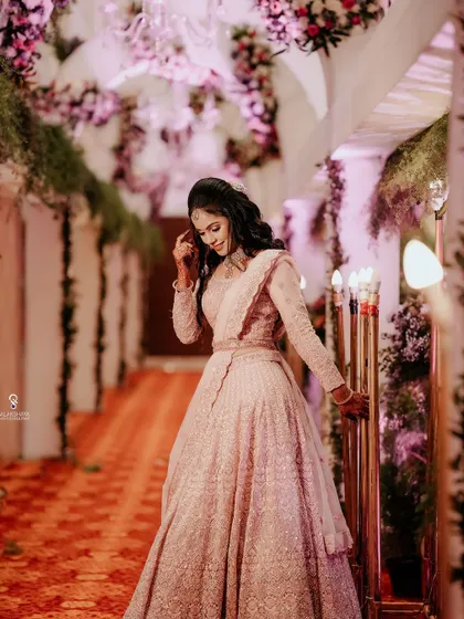 A full-length shot of a bride in a pink lehenga, captured in a beautifully decorated hallway.
