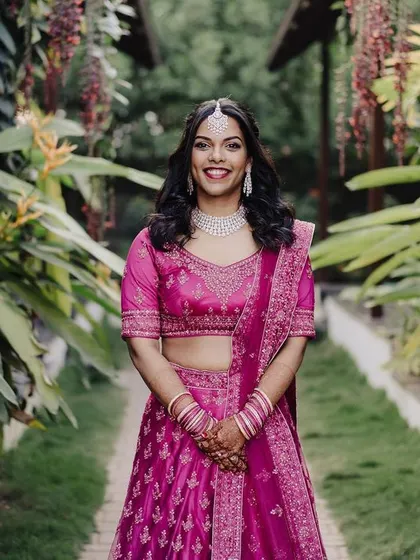 A vibrant bridal portrait in a lush garden setting. The bride's bright pink lehenga stands out beautifully against the greenery, creating a fresh and colorful image.