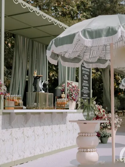 The bar area, complete with stylish umbrellas and custom-designed high tables. The front of the bar features a delicate floral pattern, tying it into the overall garden aesthetic.