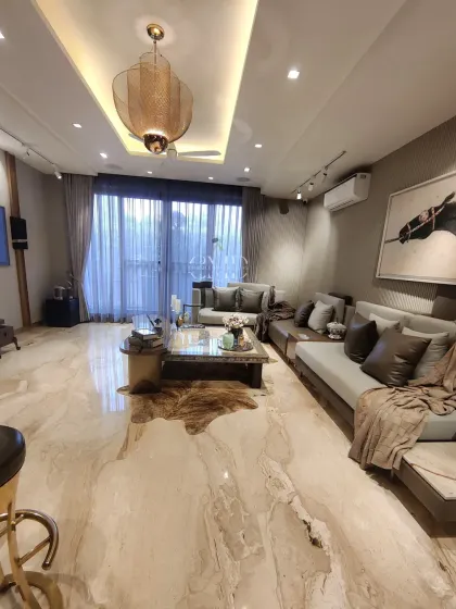 A panoramic view of the Gurgaon living area, showcasing the plush neutral sofas, marble-top coffee table, and layered lighting that balance comfort and elegance.
