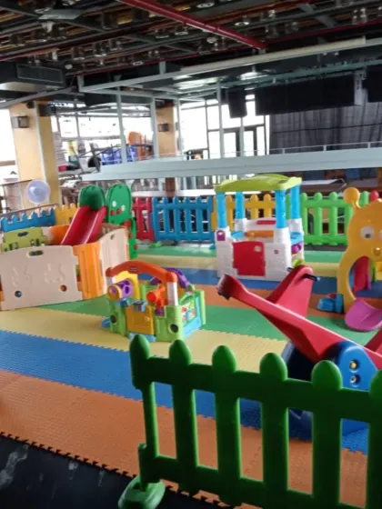 A wide-angle view of an indoor playzone set up in a large hall. The area includes multiple slides, climbers, and soft play structures, all arranged on colorful foam mats to create a safe and engaging environment for kids.