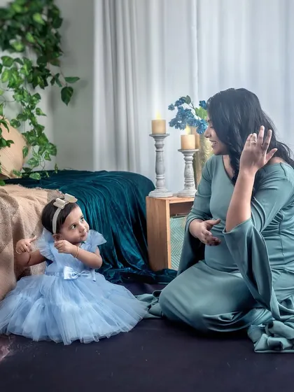 A mother-to-be sits on the floor with her young daughter in a beautifully styled boho studio. The image captures a sweet conversation between them, with the daughter looking up at her mom.