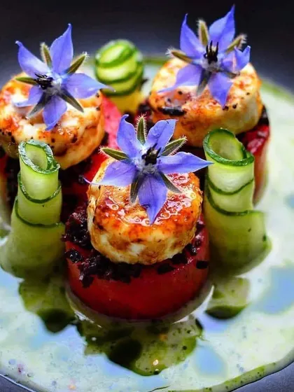 An appetizer of pan-seared paneer or cheese on a bed of stuffed tomatoes, garnished with edible borage flowers. A perfect example of our innovative vegetarian cuisine.