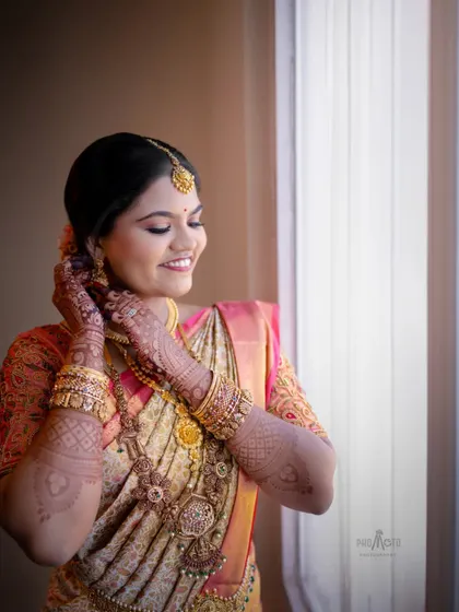 A beautiful candid of the bride adjusting her jewelry by the window, her smile full of warmth and anticipation.