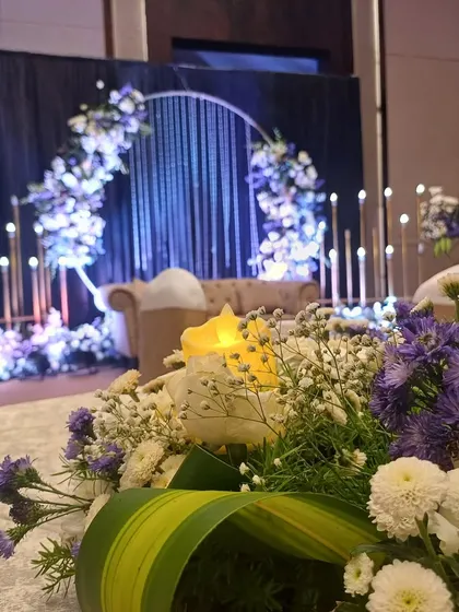 A close-up of the floral arrangements for a modern reception stage with a circular arch and candle-like lights.