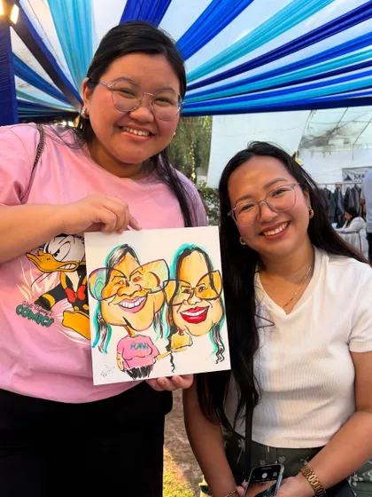 Two friends happily showing off their group caricature at the Earth Mela.